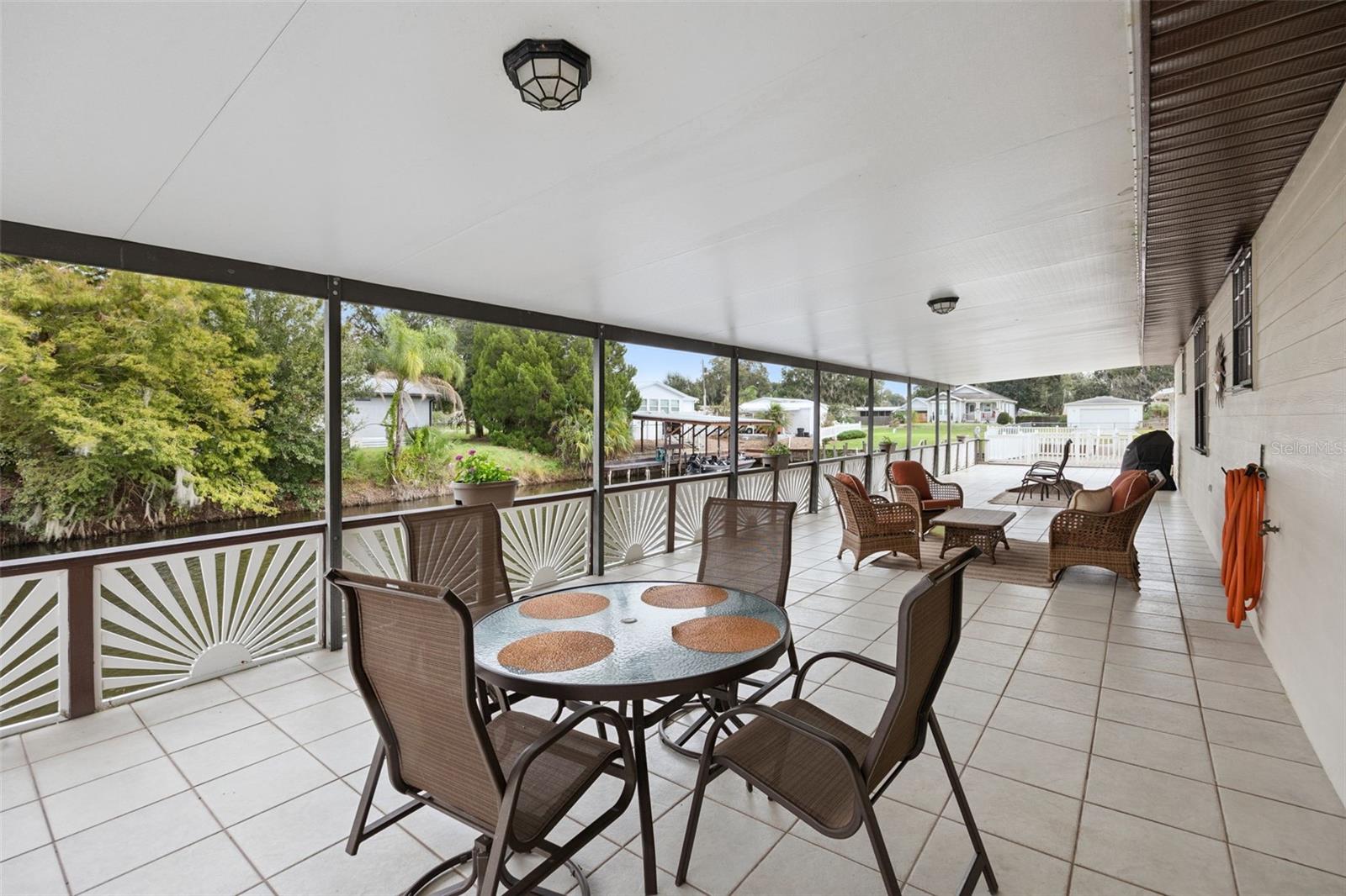 Covered Deck Dining Nook: Generous tiled covered patio setup with outdoor dining furniture facing the canal frontage.