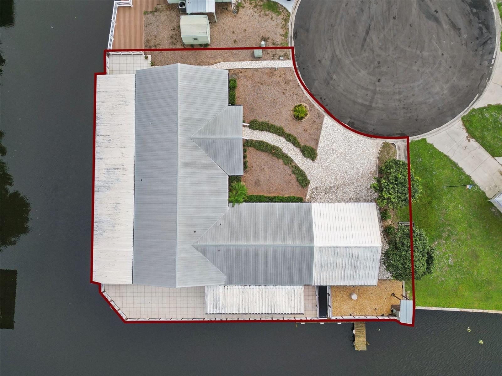 Aerial Property Boundary View: Top-down aerial photograph outlining the lot boundary, metal roof structure, and surrounding canal access.