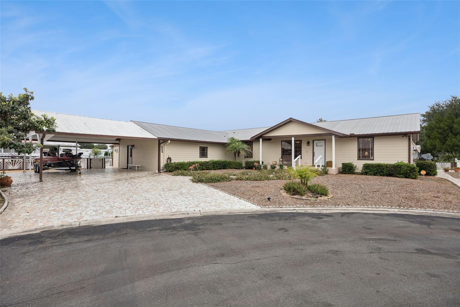 Front Elevation & Carport: Wide front perspective showcasing the extended stone driveway, large attached double carport, covered front porch, and manicured xeriscape landscaping.