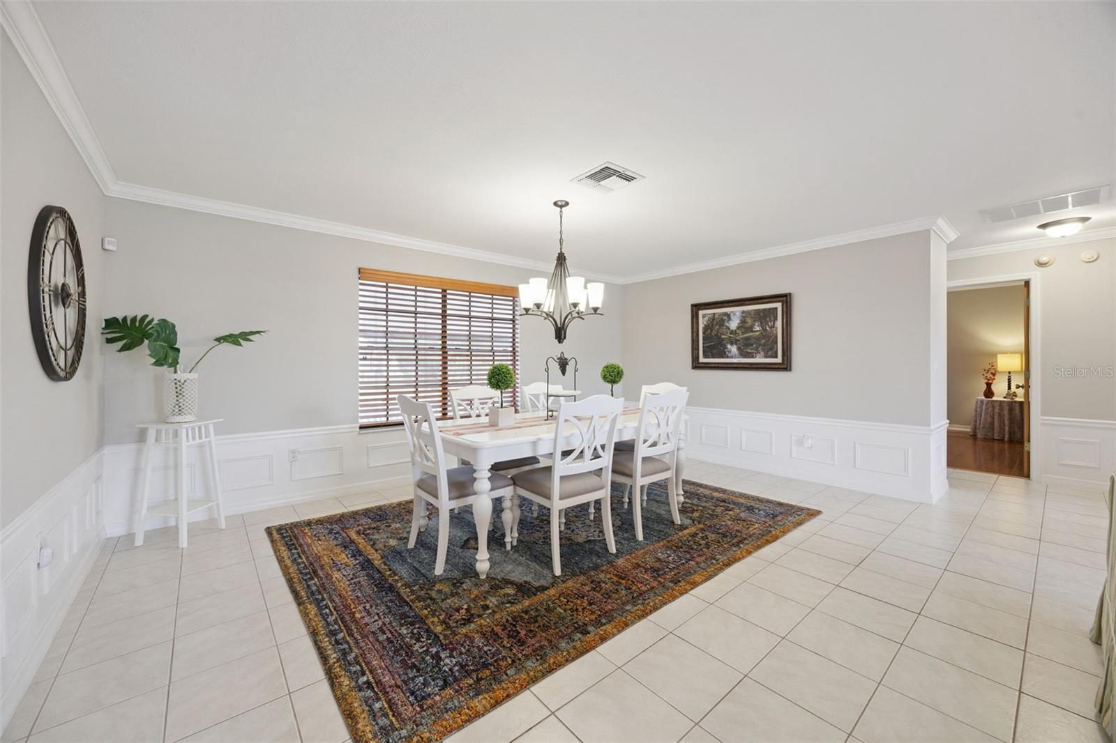 Formal Dining Room: Elegant formal dining area featuring classic wainscoting paneling, crown molding, a central chandelier fixture, and tiled flooring.