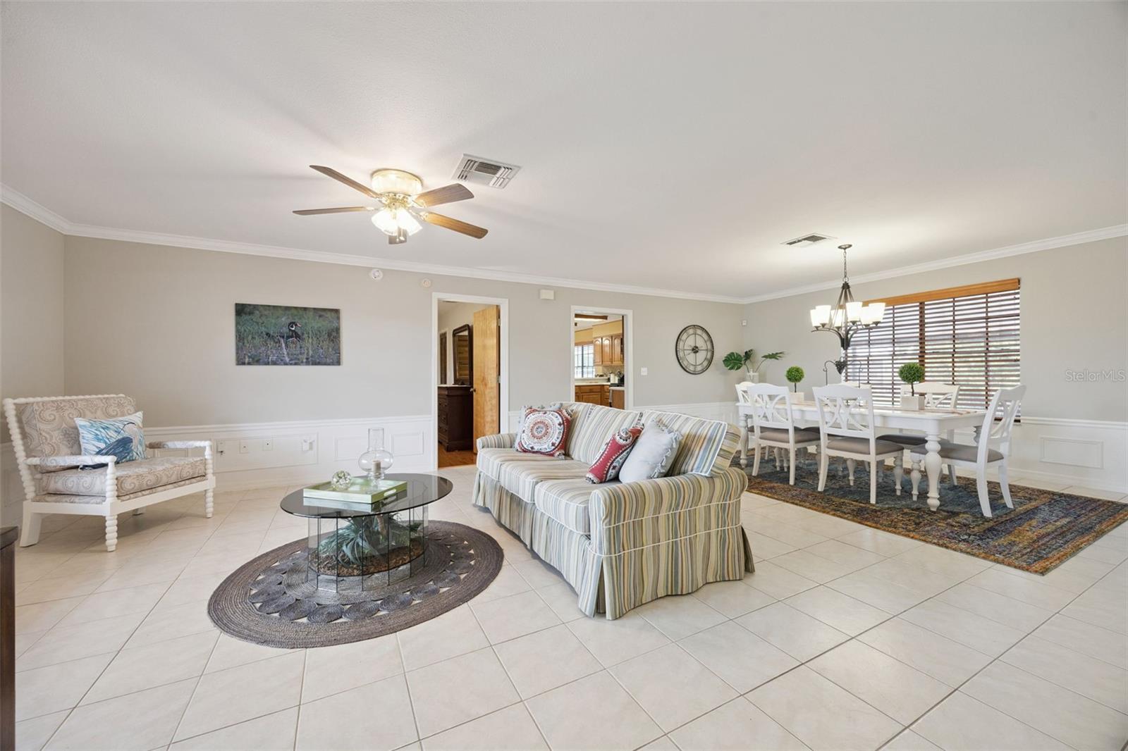 Formal Living & Dining View: Expansive great room highlighting tile flooring, detailed wainscoting, ceiling fan, and open flow into the formal dining space.