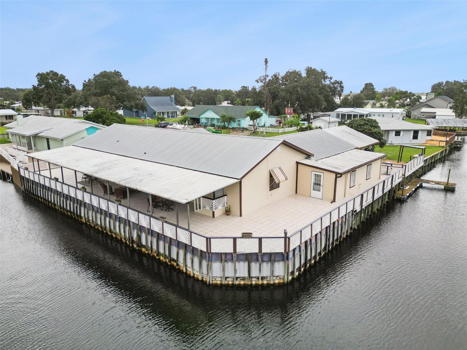 Aerial Point Lot View: Low-altitude drone shot highlighting the extensive seawall, wraparound tiled patio, and dual canal frontage.
