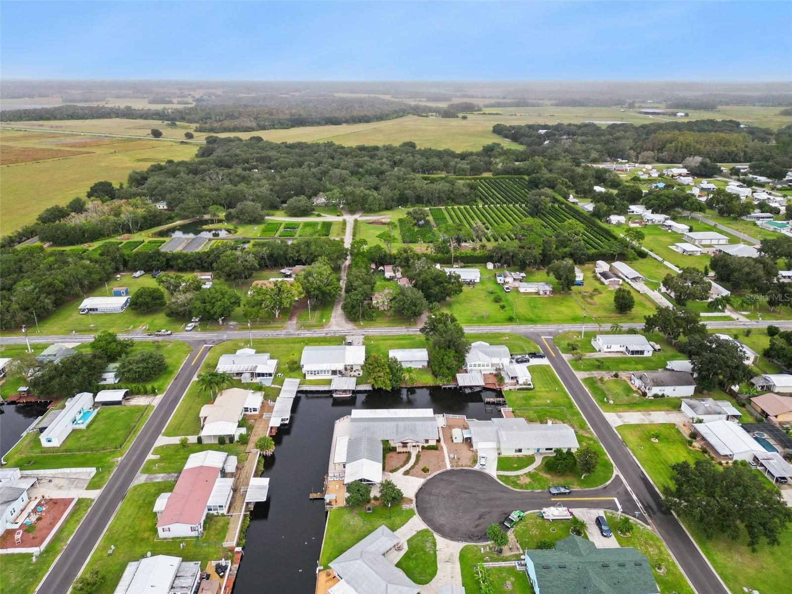 Aerial Community & Countryside View: Broad high-altitude aerial view showcasing the home's cul-de-sac position within the quiet canal community, backed by lush green pastureland.
