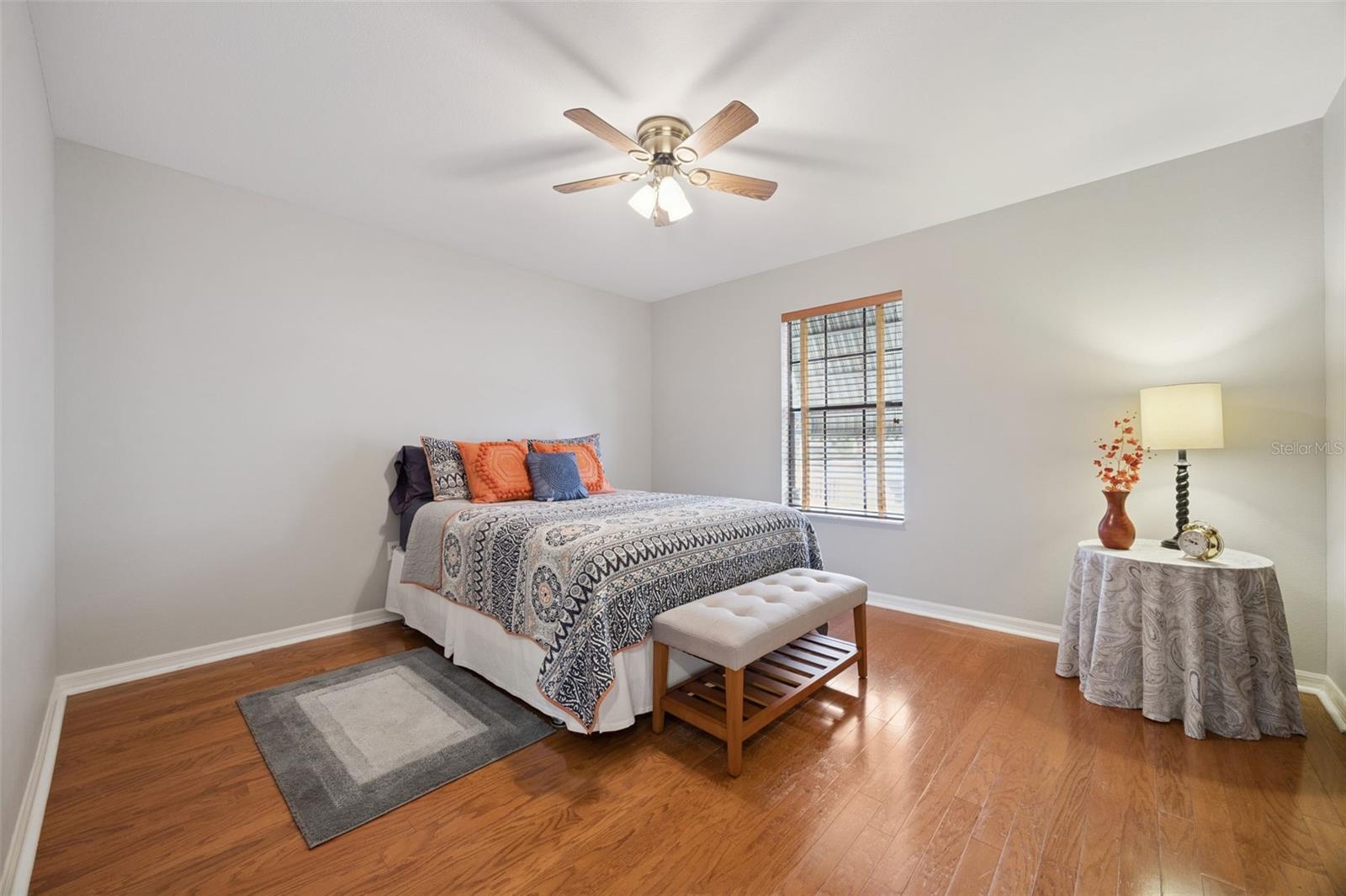 Guest Bedroom: Bright guest bedroom featuring warm wood-grain flooring, central ceiling fan, neutral wall paint, and a bright exterior window.