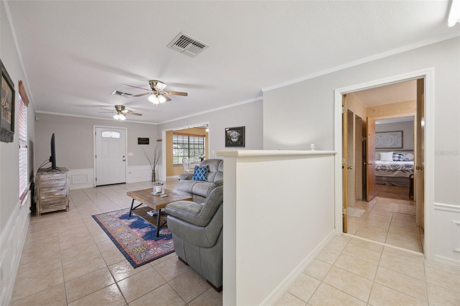 Living Room & Hall Transition: Broad living space detail showing tile floors, half-wall divider, wainscoting trim, and doorway access toward secondary rooms.