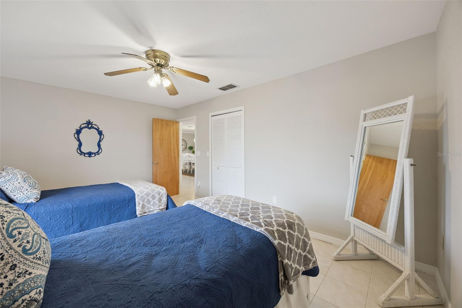 Twin Guest Bedroom: Spacious guest bedroom setup with dual twin beds, neutral tiled flooring, ceiling fan, and louvered closet doors.
