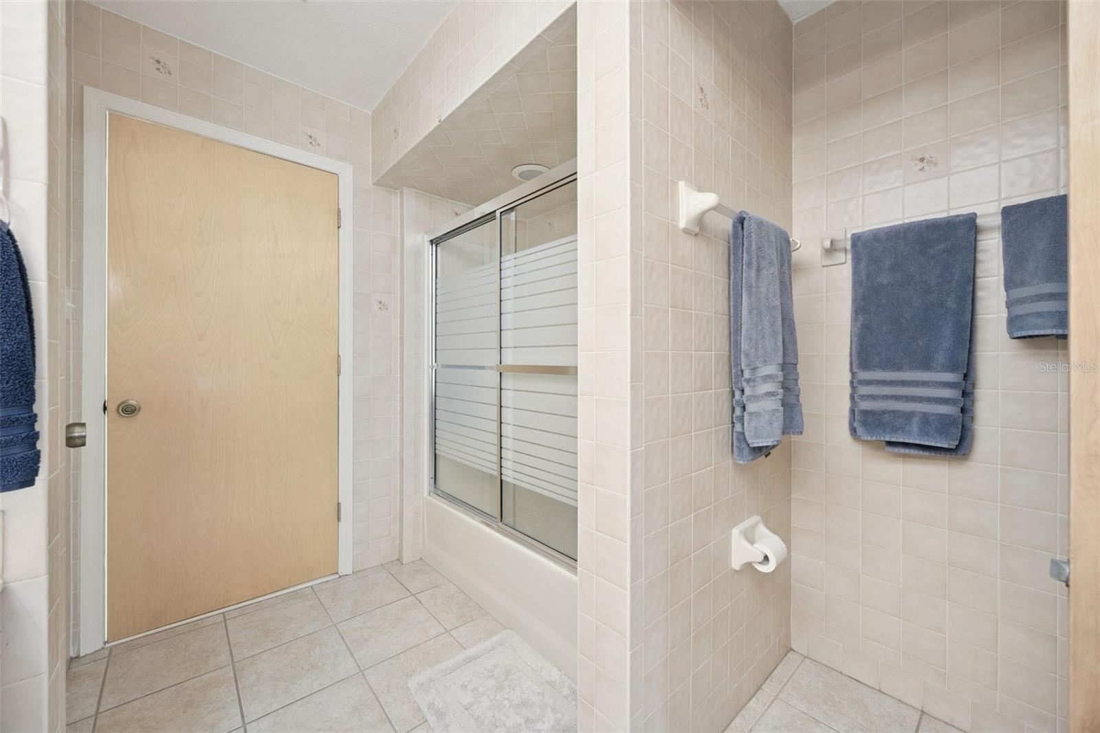 Primary Ensuite Bathroom: Tiled primary bath featuring a walk-in shower with sliding glass doors, separate vanity area, and neutral tile finish.
