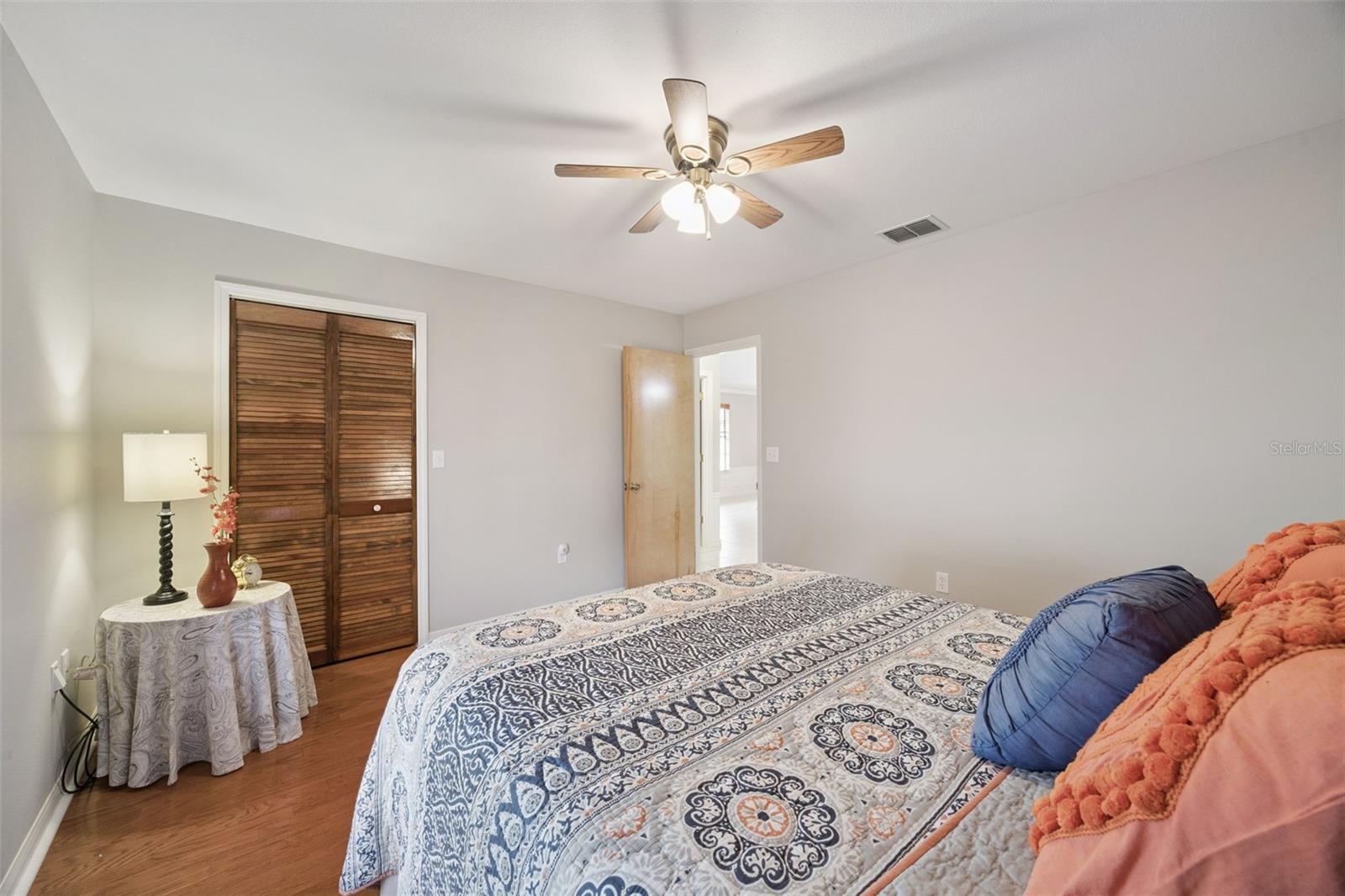 Guest Bedroom Closet: Comfortable secondary bedroom showing warm wood flooring, ceiling fan, and a built-in louvered closet.