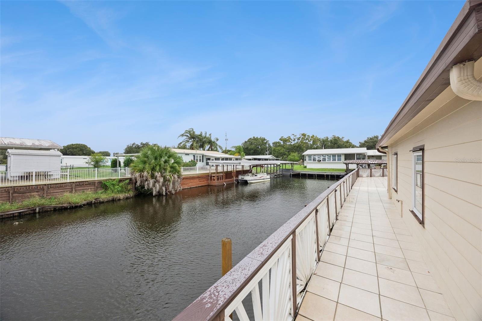 Canal Railing & Walkway View: Elevated side perspective along the tiled patio deck overlooking the canal water and neighboring docks.