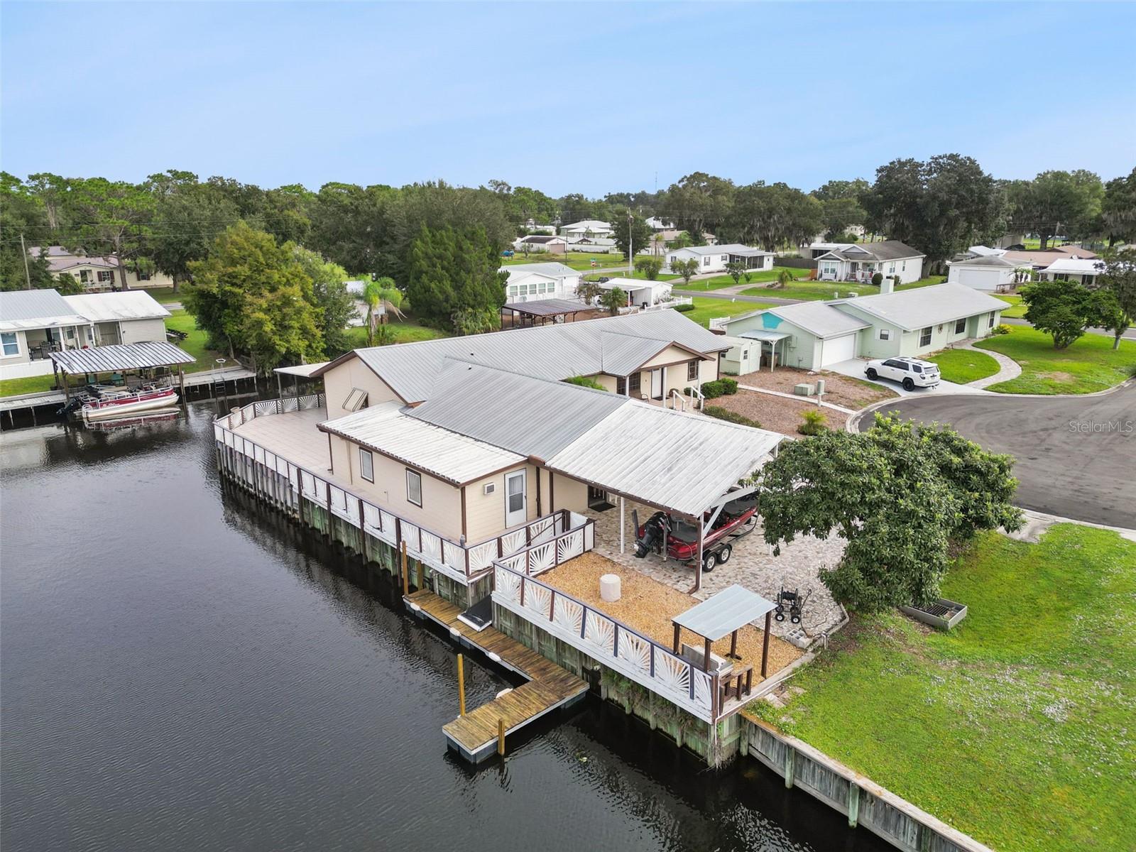 Aerial Side View & Boat Slip: Drone photo capturing the property's side dock, trailered boat carport, gravel patio area, and direct canal frontage