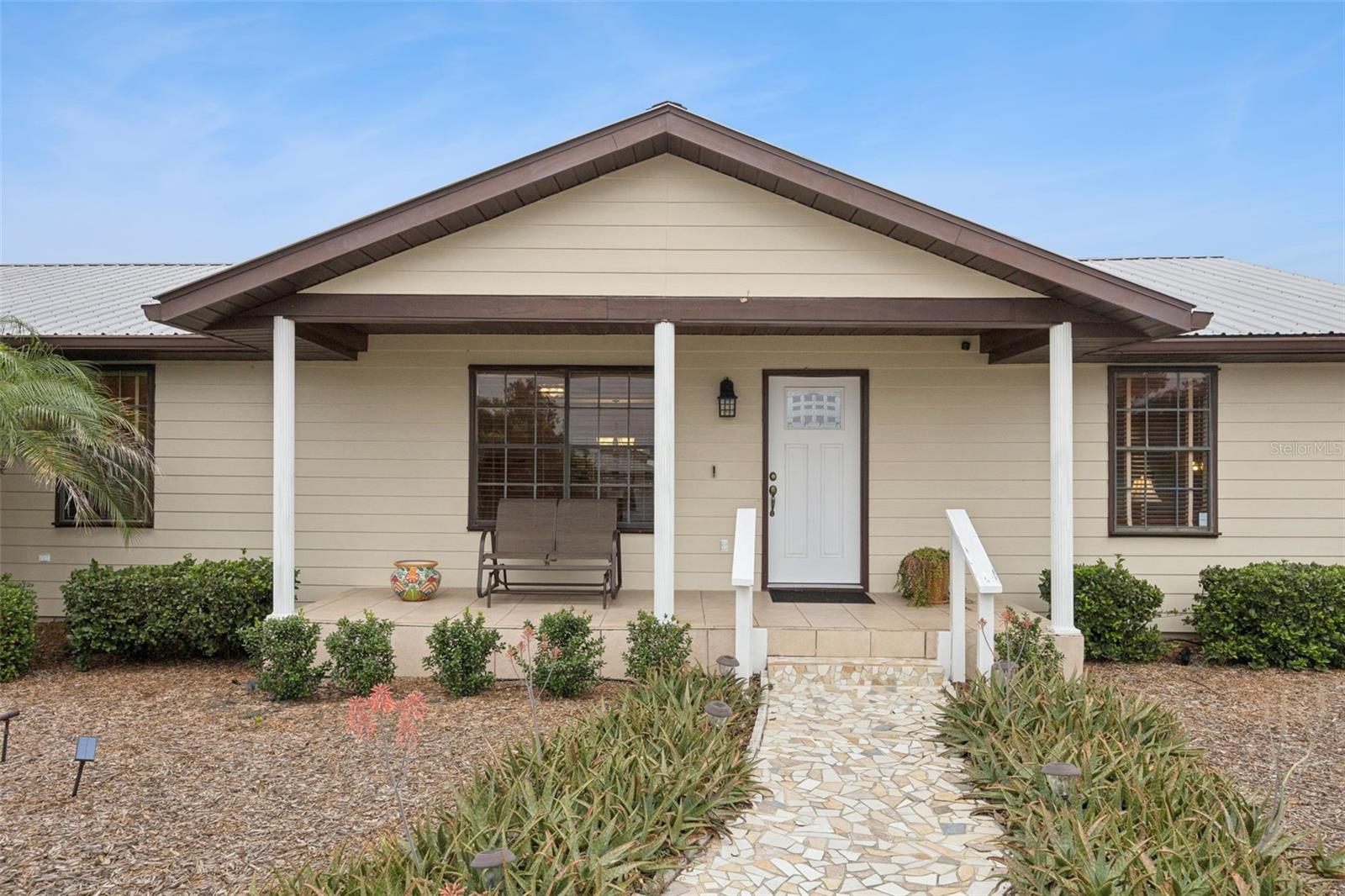 Covered Front Entry: Inviting covered front porch with decorative white support columns, tile flooring, and custom stone pathway leading to the main door.