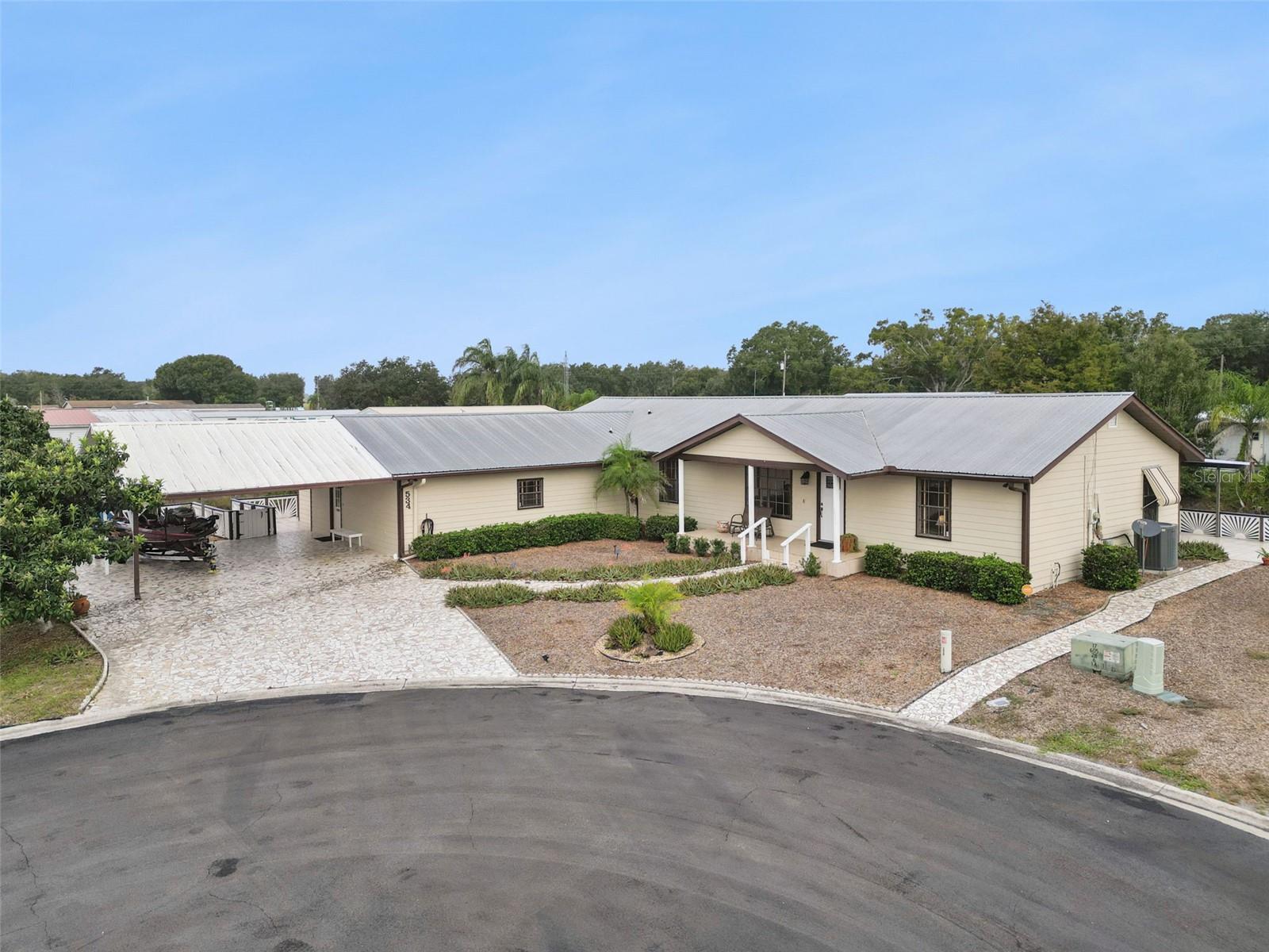 Aerial Front Street View: Elevated view highlighting the spacious lot, wide cul-de-sac positioning, long stone driveway, and generous covered parking space.