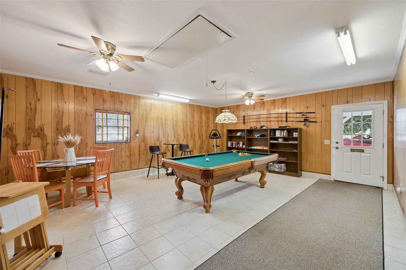 Game Room / Recreation Space: Massive game room featuring wood panel walls, tiled flooring, ceiling fans, pool table area, and direct exterior door access.