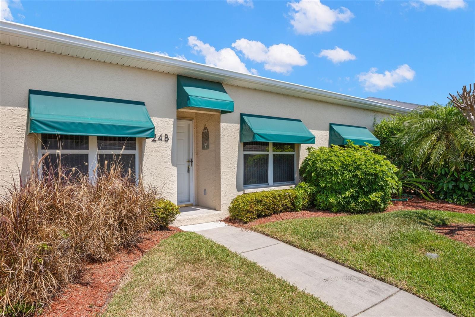 Charming front exterior with manicured landscaping, green awnings, and a private covered entry, creating a welcoming first impression.
