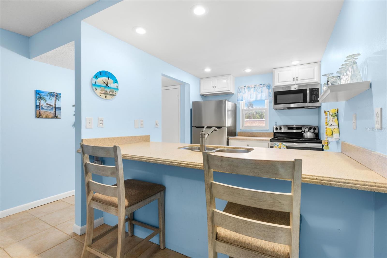 The kitchen wraps around a broad Corian breakfast bar with seating for two, with recessed lighting, a window over the rear counter and stainless-steel appliances including the refrigerator, range and microwave.
