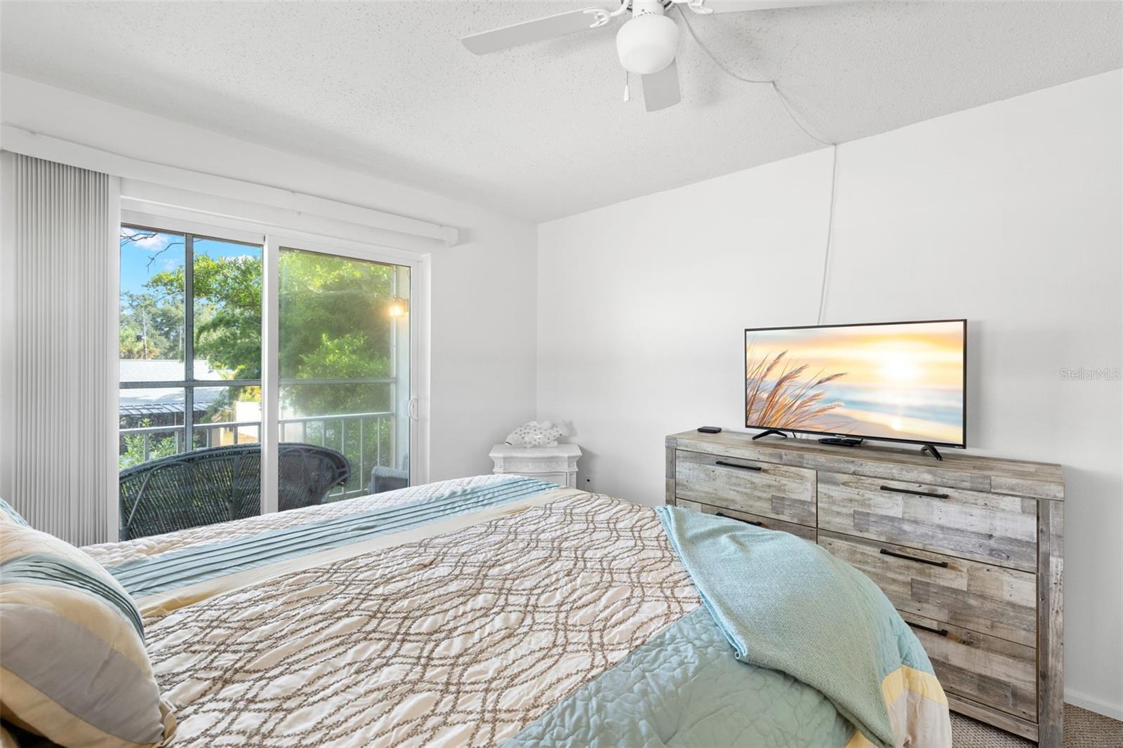 The primary bedroom measures approximately 14'9" x 11'3", with a ceiling fan overhead and sliding glass doors opening directly to the screened balcony and its leafy outlook.