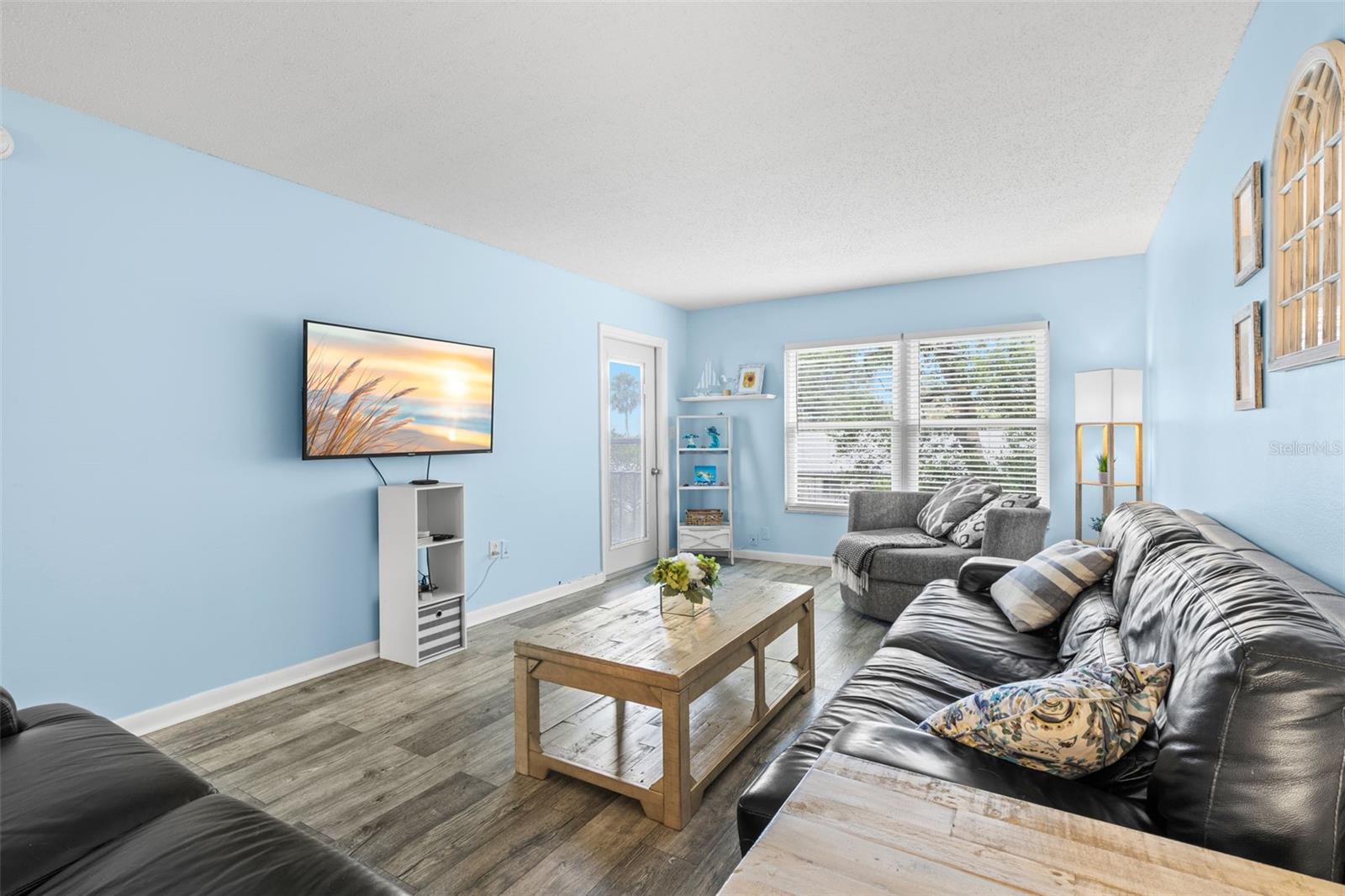 At the far end of the living room, a broad window and a door to the screened balcony bring in natural light, while the rooms long proportions leave plenty of space for substantial seating and media furniture.