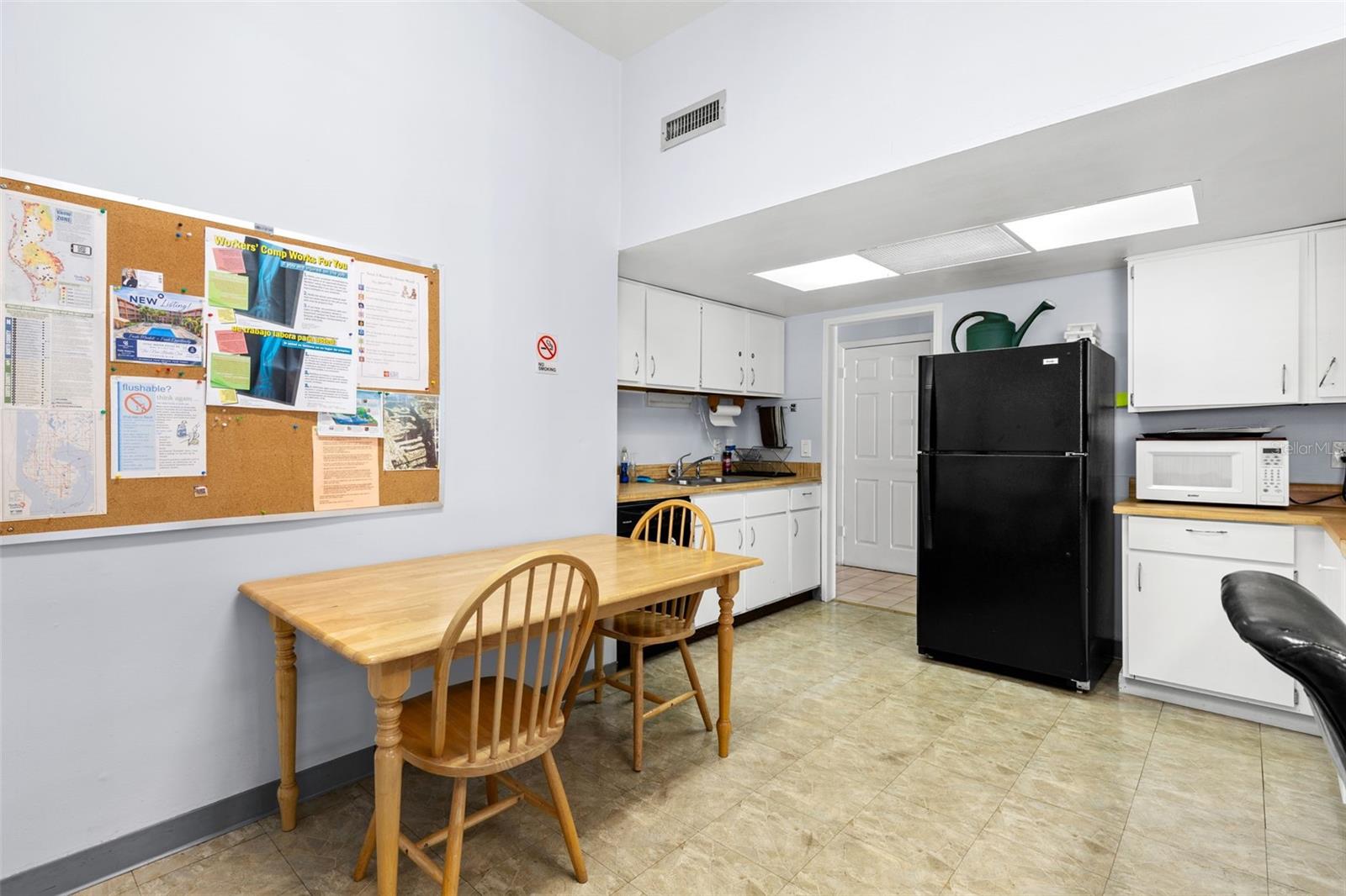 The clubhouse includes a community kitchen with full-size refrigerator, microwave, sink, cabinetry and table seating, providing space for gatherings and shared activities.