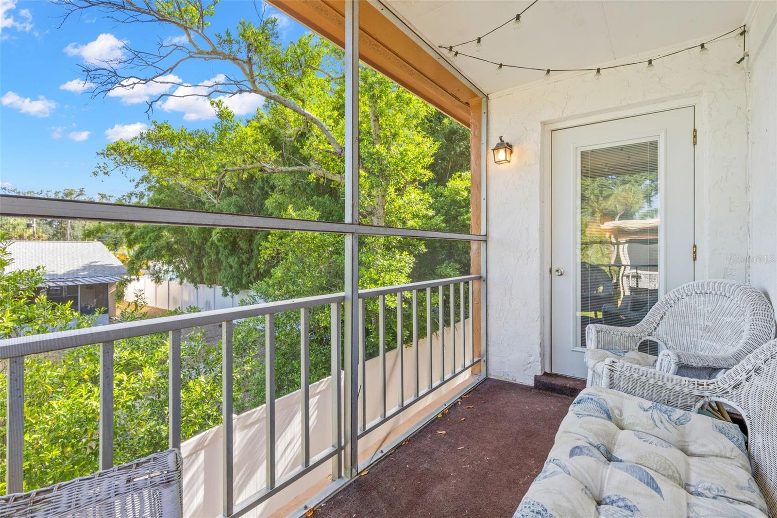 Positioned between the living room and primary bedroom, the screened balcony creates a comfortable outdoor extension of both spaces, with room for seating and a leafy view framed by mature trees.