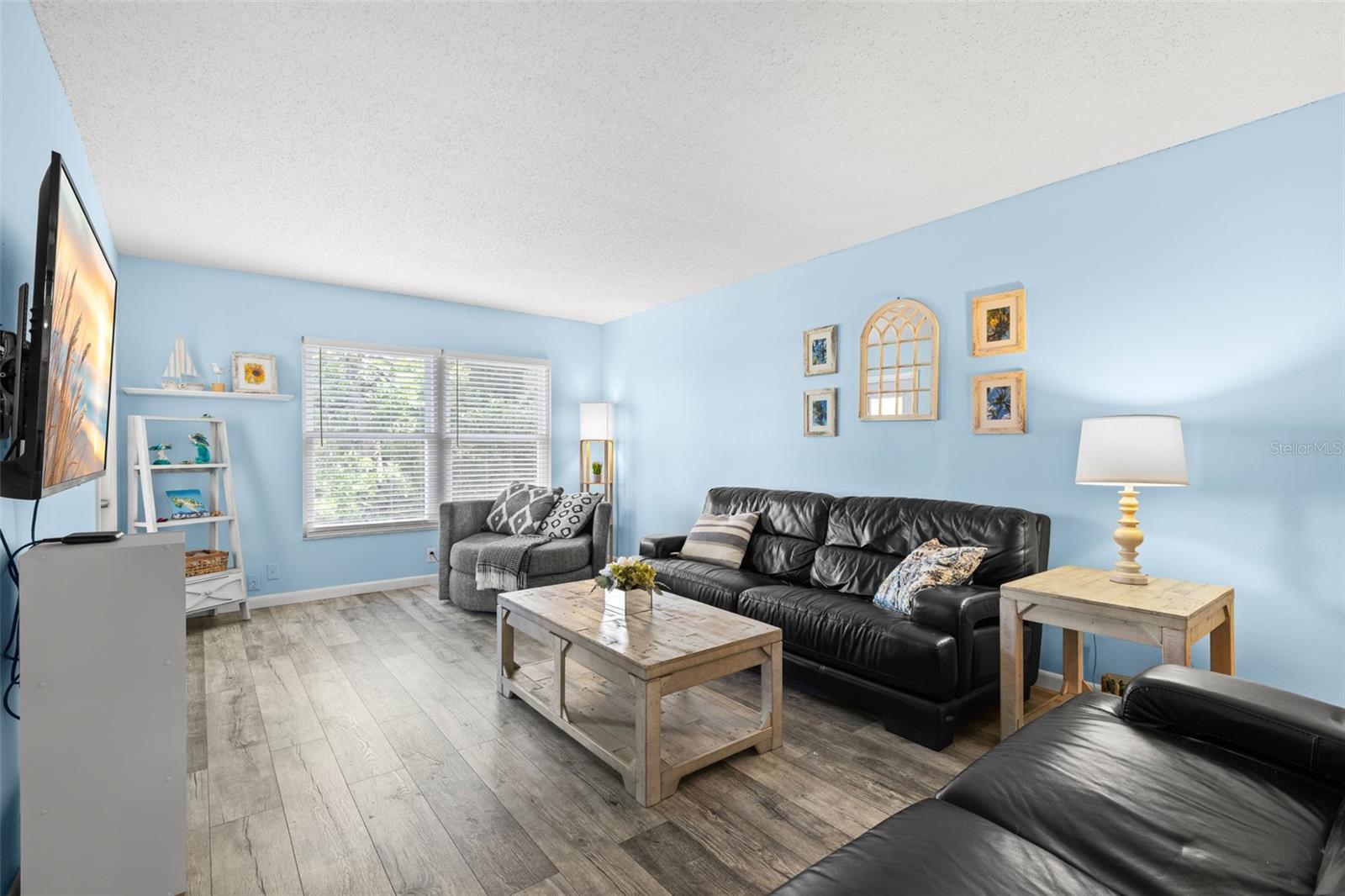 The 20-foot living room offers plenty of space for a full seating arrangement, with luxury vinyl flooring and a wide bank of windows drawing natural light across the room.