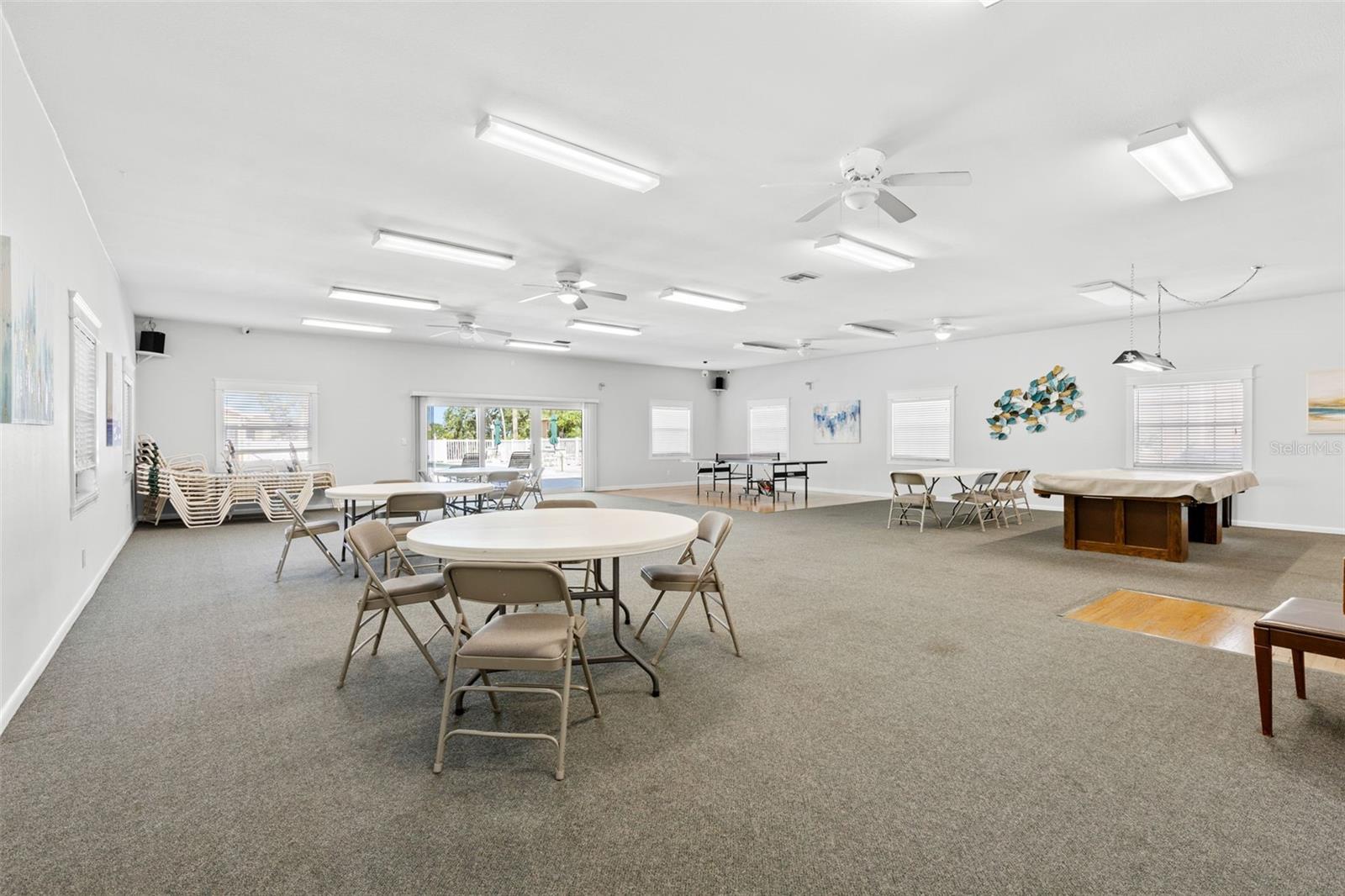 The clubhouse provides plenty of room to gather, with multiple tables for cards or games, billiards and ping-pong, plus doors opening toward the pool area.