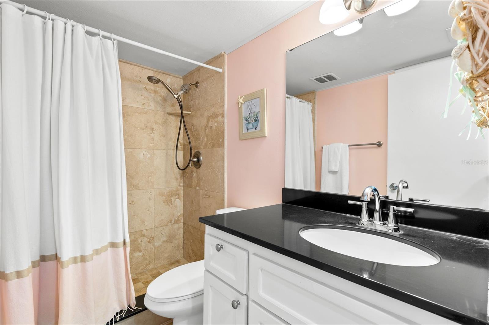 The bath pairs a dark countertop with light cabinetry and a large mirror, while the tub/shower is finished with tile surround and a handheld showerhead.