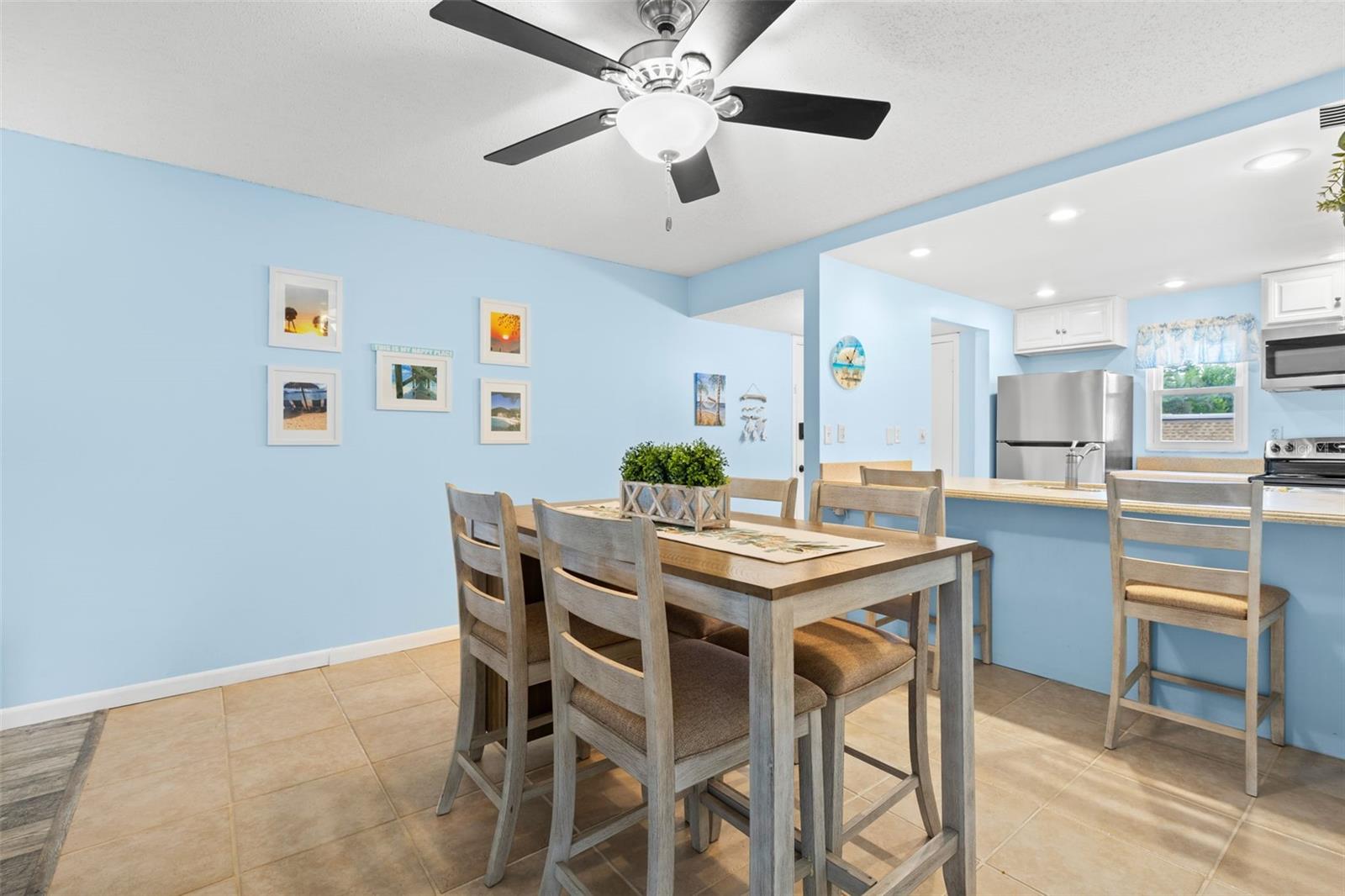 The dining area sits just beyond the kitchen, with tile flooring, a ceiling fan overhead and enough room for a full dining set, while the breakfast bar adds extra seating along the kitchen edge.