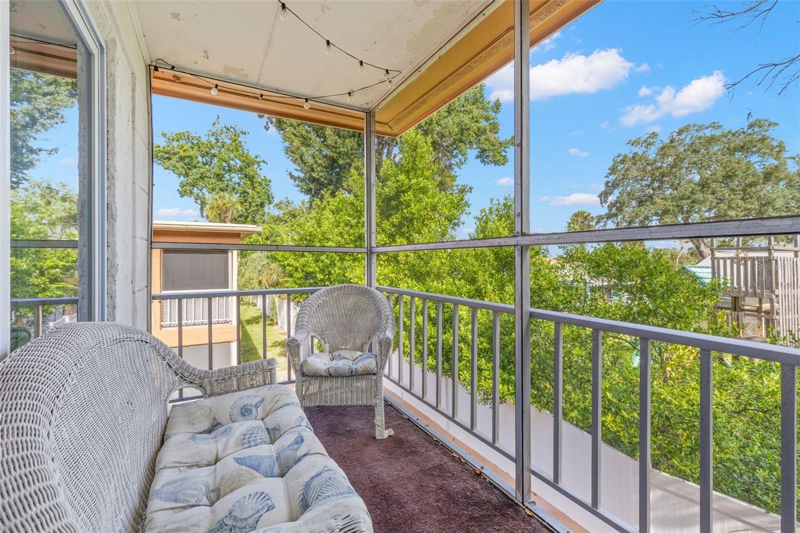 The screened balcony extends the living space outdoors, with room for seating and a leafy outlook framed by mature trees and open sky.