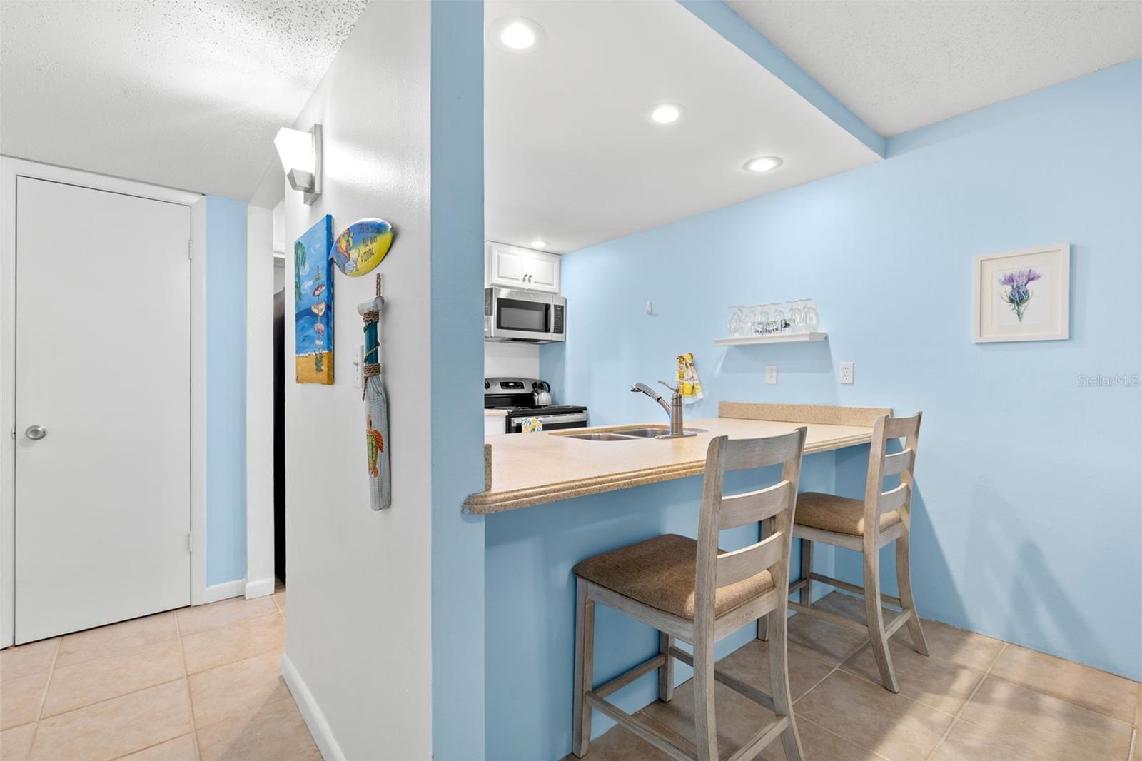 A closer look from the dining area shows the breakfast bar with seating for two, while the kitchens recessed lighting, Corian counters and open pass-through keep the space bright and connected to the rest of the condo.