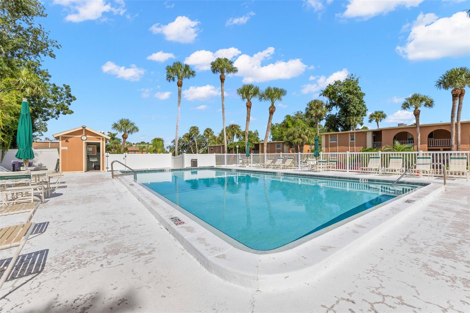 One of the community pools offers a spacious deck with plenty of lounge seating and umbrellas, framed by tall palms and the surrounding residential building.