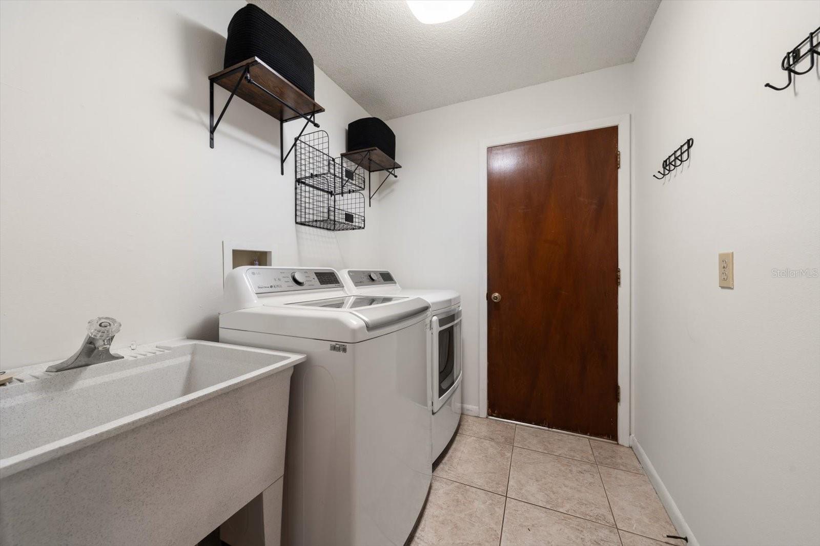 Update laundry room with sink and shelving and access to the large garaage with tiled flooring and a workshop area.