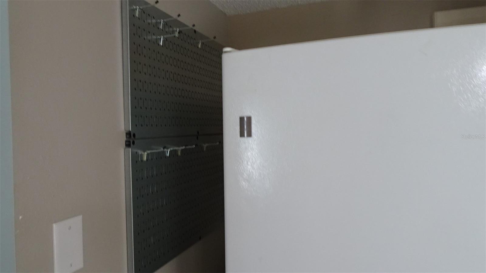 Pegboard with hooks next to refrigerator for pots and pans and whatnots.