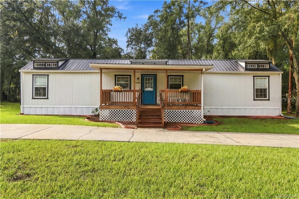 Front Elevation  Enjoy the home's charming curb appeal, featuring a welcoming covered porch, wooden railings, decorative roof details & circular concrete driveway.