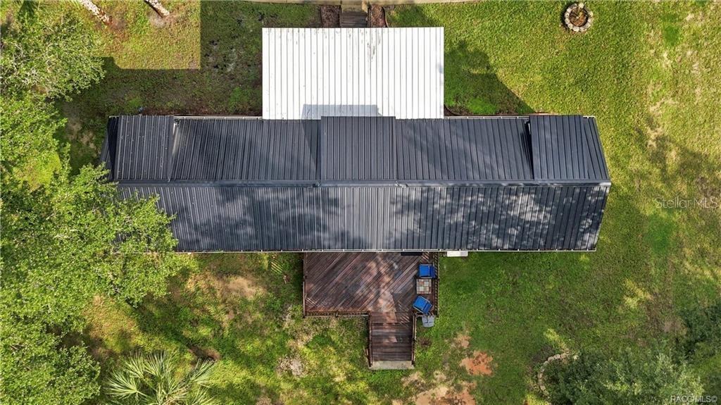 Aerial Roof & Deck View  Bird's-eye perspective showcasing the METAL ROOF, covered front porch, spacious WOODEN REAR DECK & surrounding green space.