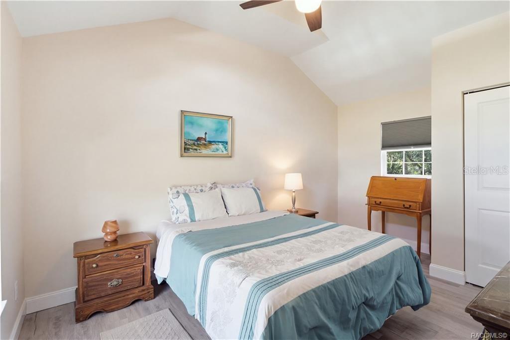 Primary Bedroom  Cozy & inviting bedroom featuring VAULTED CEILINGS, luxury vinyl plank flooring, ceiling fan & coastal-inspired furnishings.