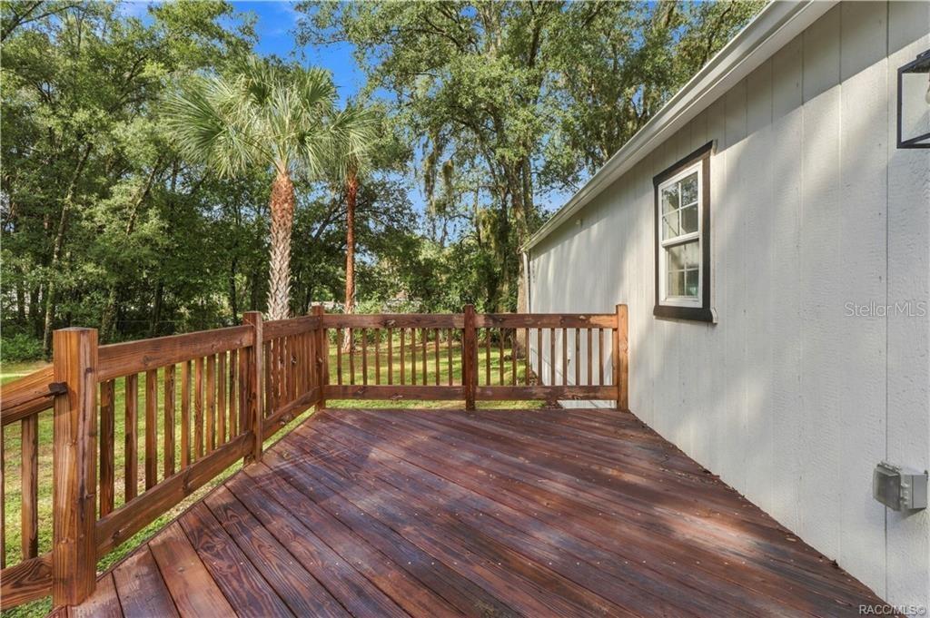 Rear Deck  Spacious wooden deck featuring sturdy railings & room for outdoor seating, surrounded by Florida greenery & mature palms.