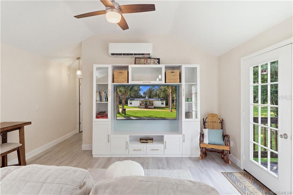 Living Room  Bright & inviting living room featuring VAULTED CEILINGS, luxury vinyl plank flooring, ceiling fan, w/entertainment cabinetry & a MINI-SPLIT HEATING & COOLING SYSTEM. French doors provide views of the backyard & access to the rear deck.