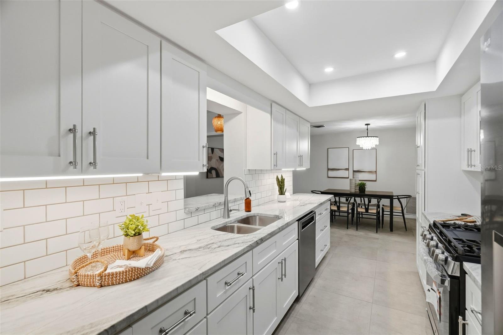 Anchoring the home is a centrally located kitchen featuring classic white shaker-style cabinetry, a subway tile backsplash, stone countertops, and a tray ceiling with recessed lighting. Anchoring the home is a centrally located kitchen featuring classic white shaker-style cabinetry, a subway tile backsplash, stone countertops, and a tray ceiling with recessed lighting.