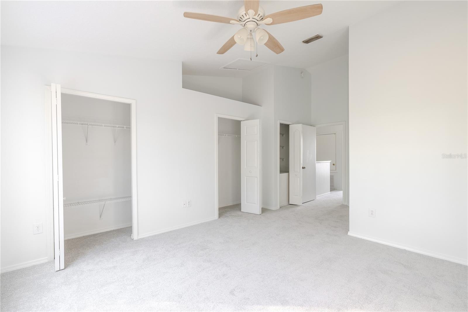 The Primary bedroom  features neutral tone walls and carpet, a ceiling fan with light kit and vaulted ceiling.