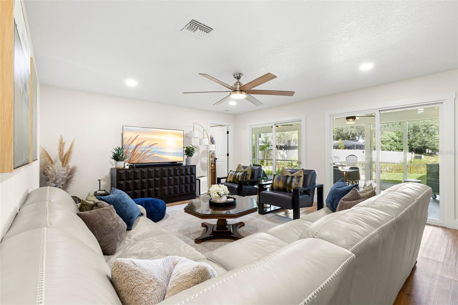 The spacious living room offers plenty of room for comfortable seating and entertaining, with recessed lighting, a contemporary ceiling fan, luxury vinyl flooring, and two sets of sliding glass doors that fill the space with natural light and provide access to the screened porch.
