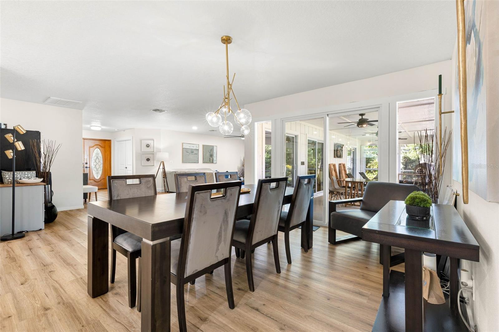 The beautifully appointed dining area features a striking contemporary gold chandelier with glass globe shades, creating an elegant focal point. Generous proportions accommodate a large dining table, while sliding glass doors provide natural light and access to the screened outdoor living area.