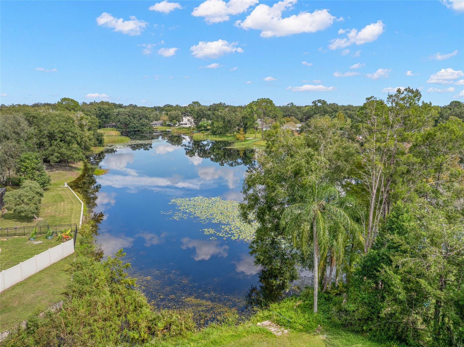 Enjoy the natural beauty of a peaceful waterfront setting, where the pond stretches beyond the backyard, framed by mature trees, lush greenery, and beautiful reflections on the water.