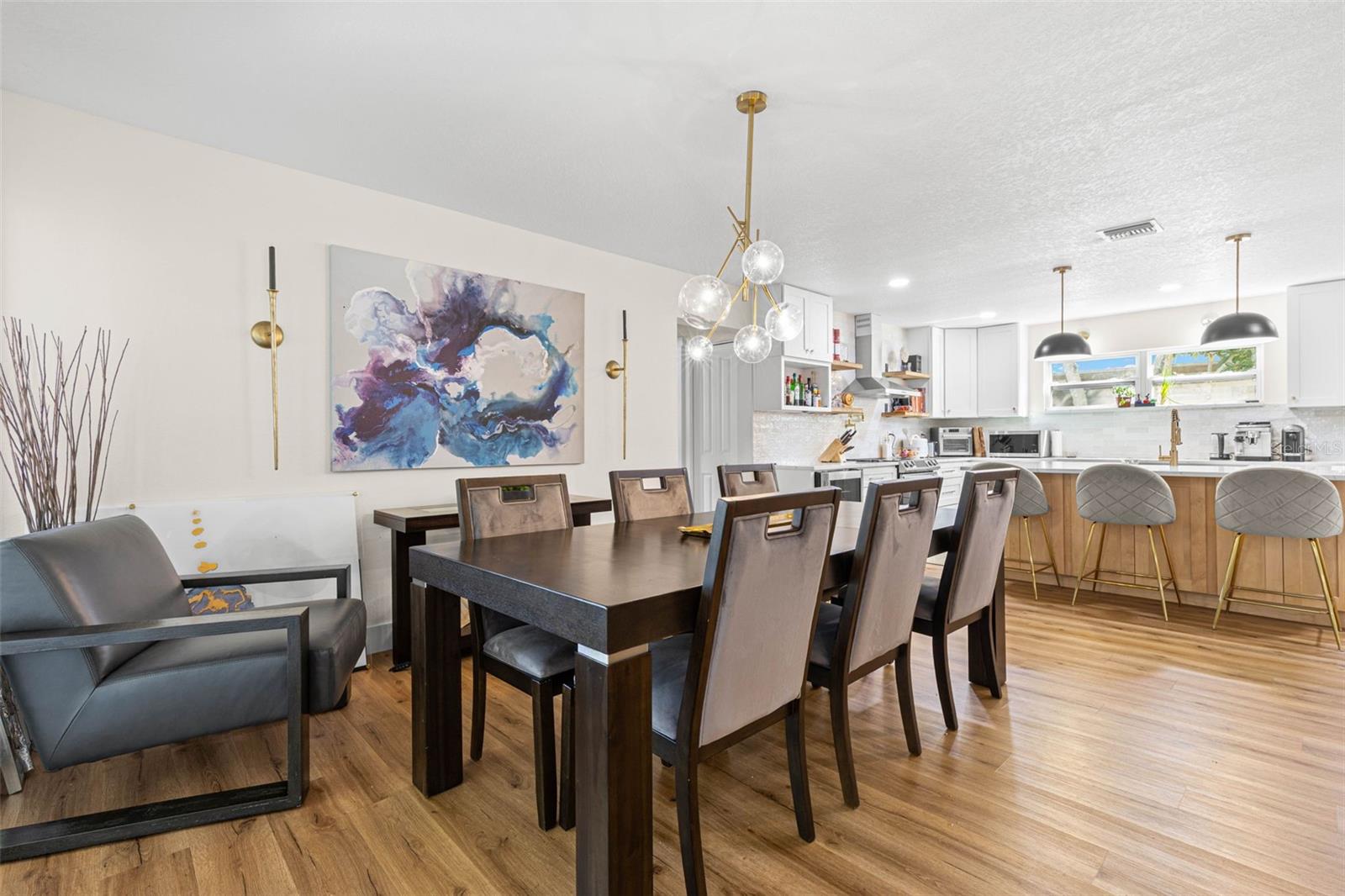 The dining area flows effortlessly into the beautifully updated kitchen, creating an ideal setting for everyday meals and entertaining. A contemporary glass-globe chandelier complements the kitchen's gold fixtures, pendant lighting, and inviting breakfast bar with seating for four.