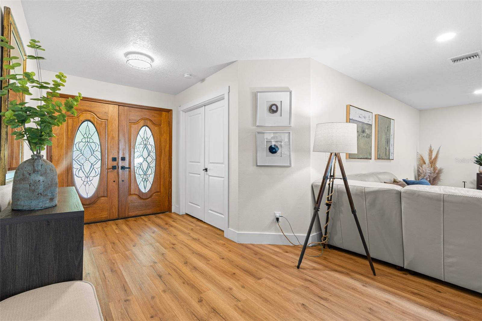 Step inside to a bright, welcoming entryway featuring decorative double doors with leaded-glass inserts, beautiful wood-look luxury vinyl flooring, recessed lighting, and a convenient entry closet. The open layout offers an inviting glimpse into the spacious living area.
