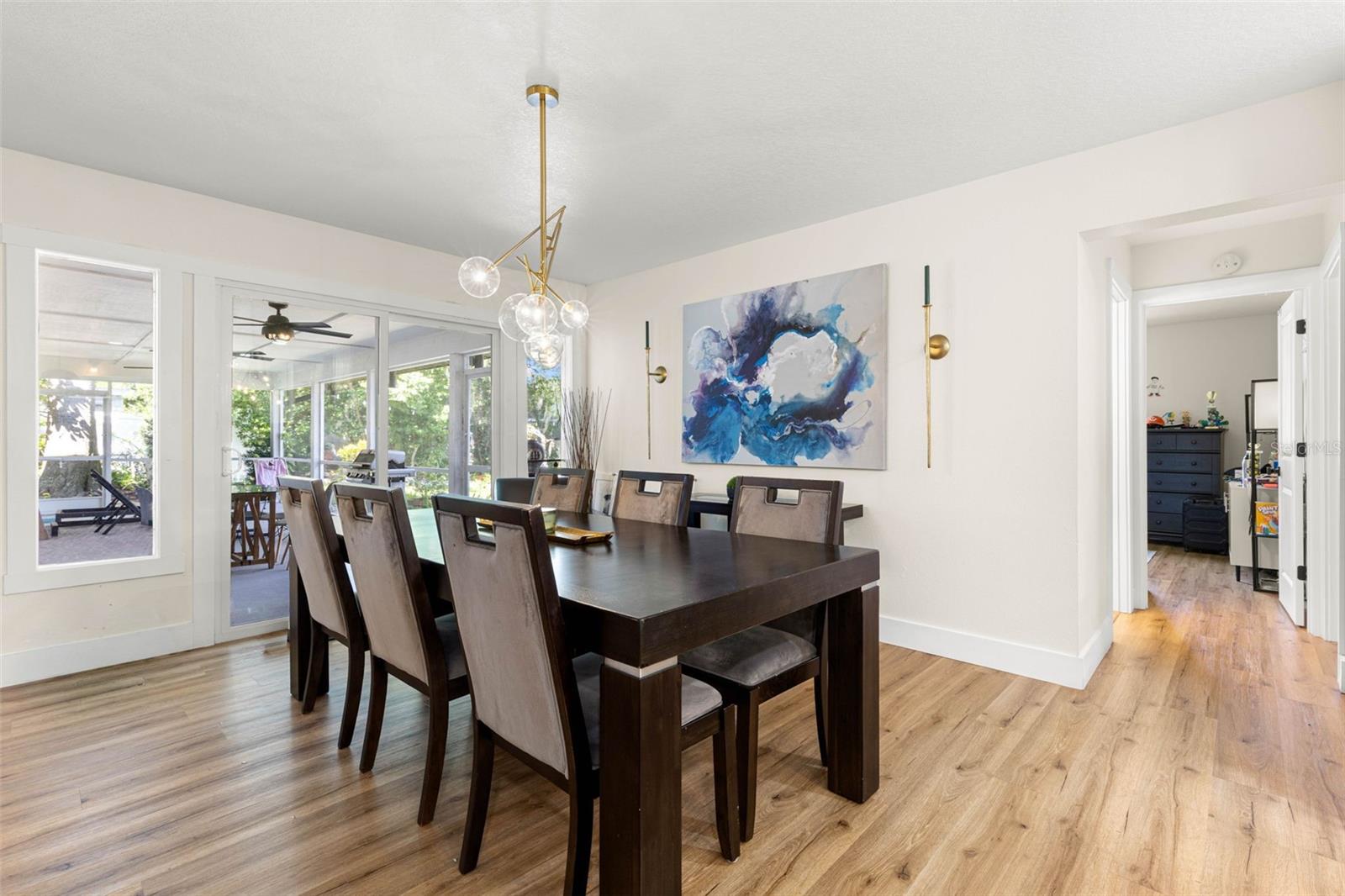 The inviting dining area comfortably accommodates a large table for gatherings and special occasions. Sliding glass doors open to the screened porch, extending the entertaining space outdoors, while an elegant gold chandelier and coordinating wall sconces add a sophisticated touch.