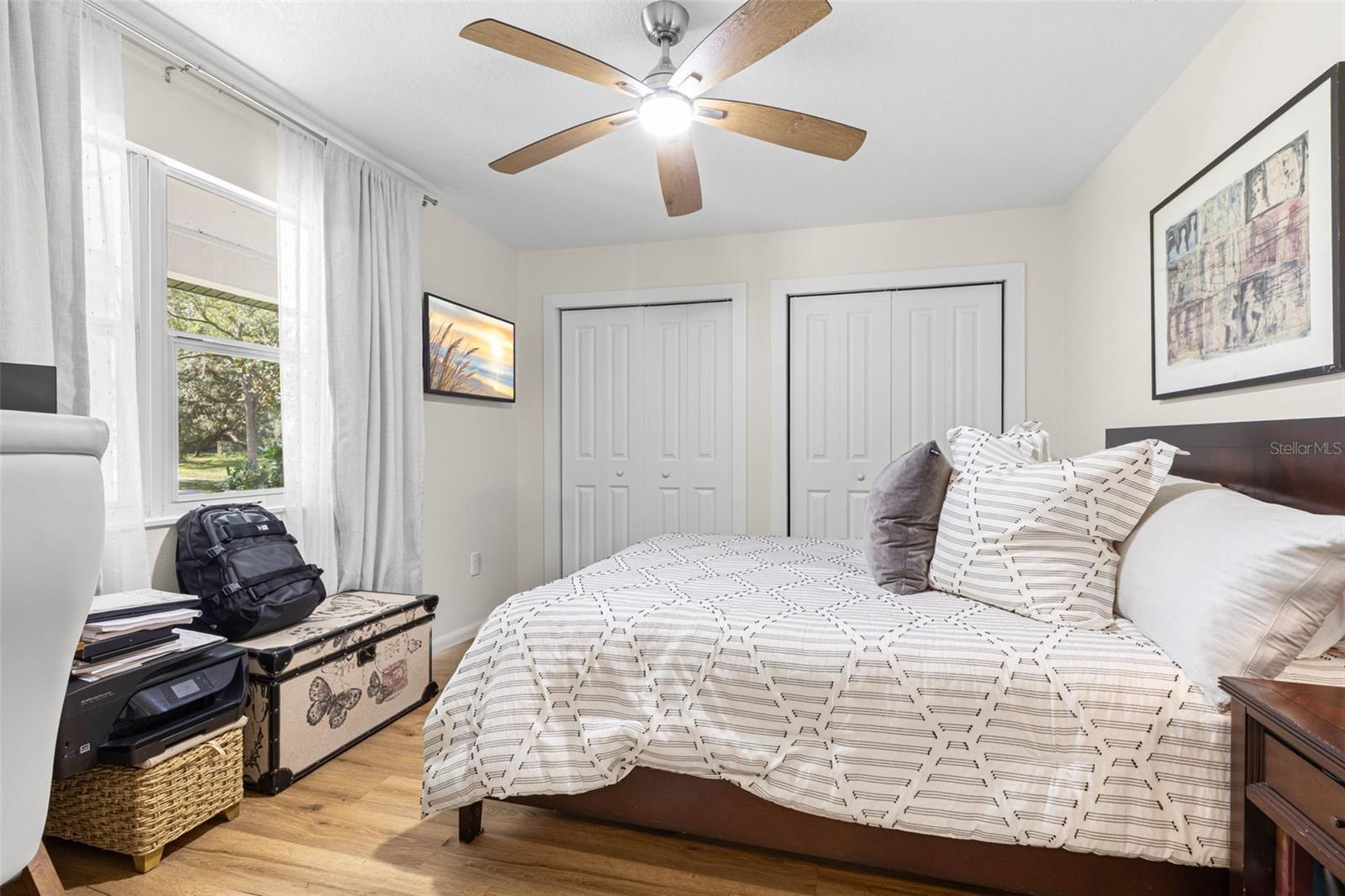 Bedroom four features two closets for ample storage, wood-look luxury vinyl flooring, a modern ceiling fan, and a window overlooking the front yard. A versatile room equally suited for guests, a home office, or a personal retreat.