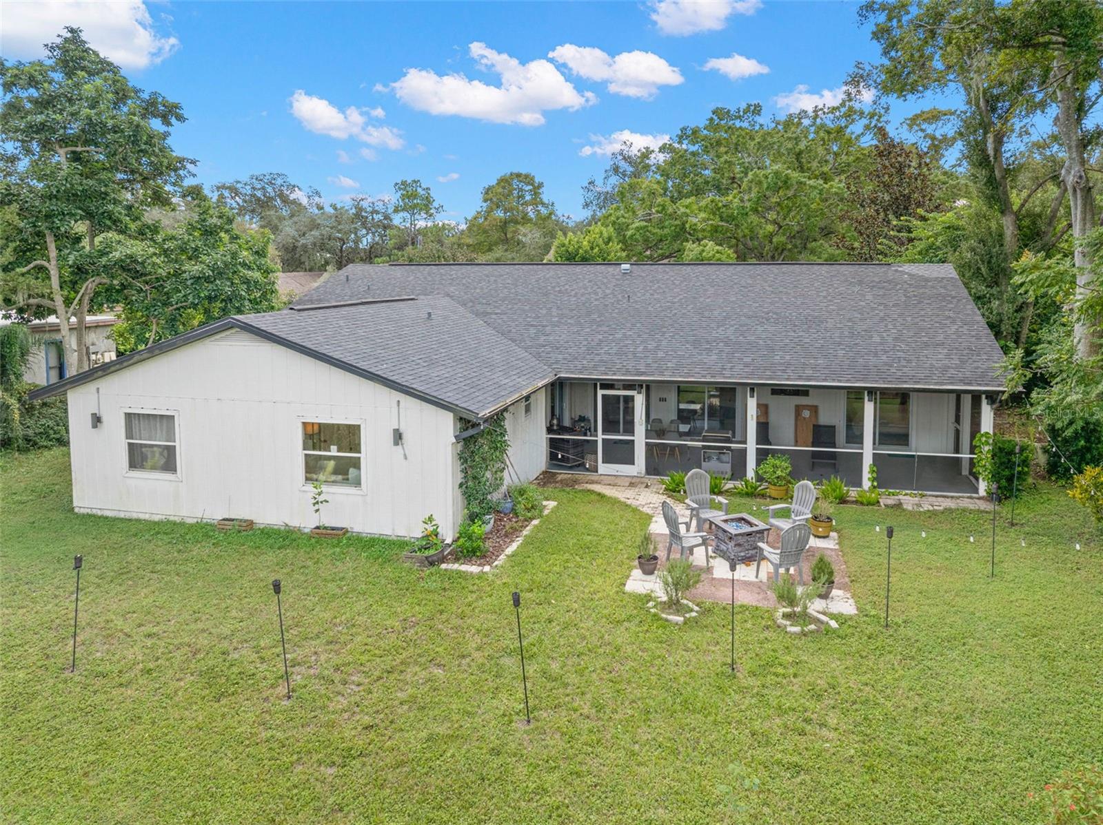 An aerial perspective showcases the home's expansive backyard, mature surrounding trees, and impressive screened porch extending across the rear of the residence. A dedicated patio and fire pit area adds another inviting outdoor gathering space, with plenty of lawn to enjoy.