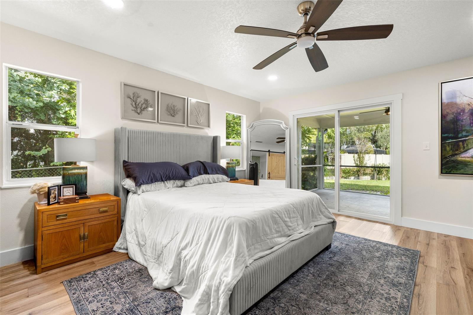 The primary bedroom offers a relaxing retreat with abundant natural light from multiple windows and sliding glass doors that open directly to the screened porch. Enjoy easy access to the outdoors, wood-look luxury vinyl flooring, and a contemporary ceiling fan.