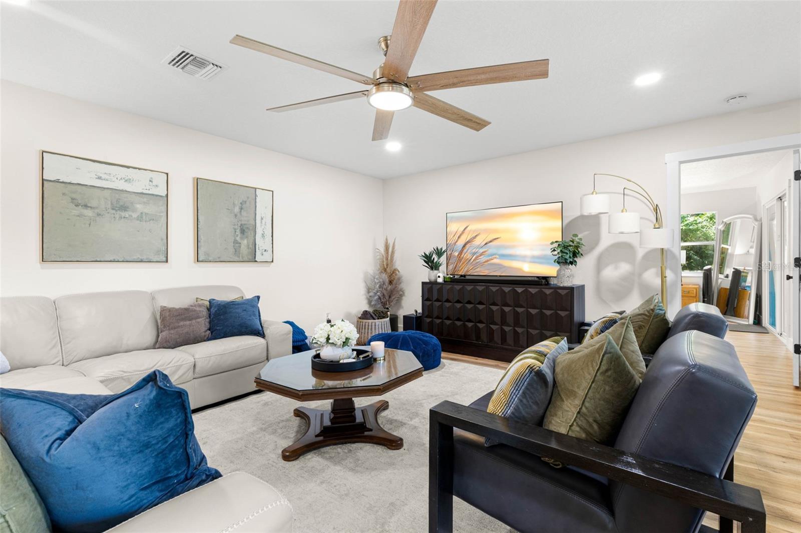 Another perspective of the spacious living room highlights its comfortable layout, generous seating area, recessed lighting, and contemporary ceiling fan with wood-tone blades. An inviting space for relaxing with family or entertaining guests.