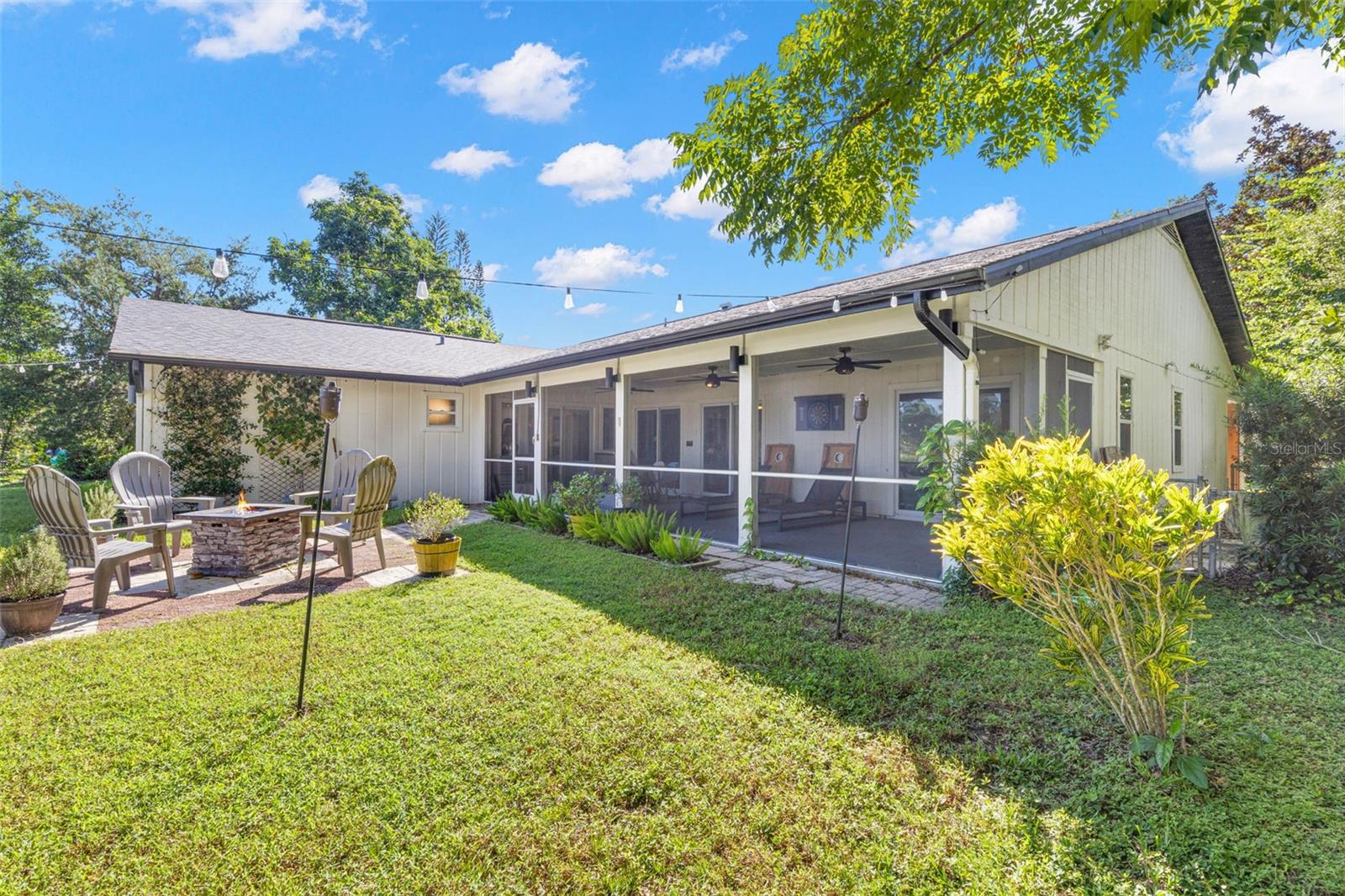 The beautifully landscaped backyard offers multiple opportunities for outdoor enjoyment, from the expansive screened porch to the open-air patio and fire pit area. Mature trees, colorful plantings, and overhead string lighting create an inviting setting for relaxing or entertaining.